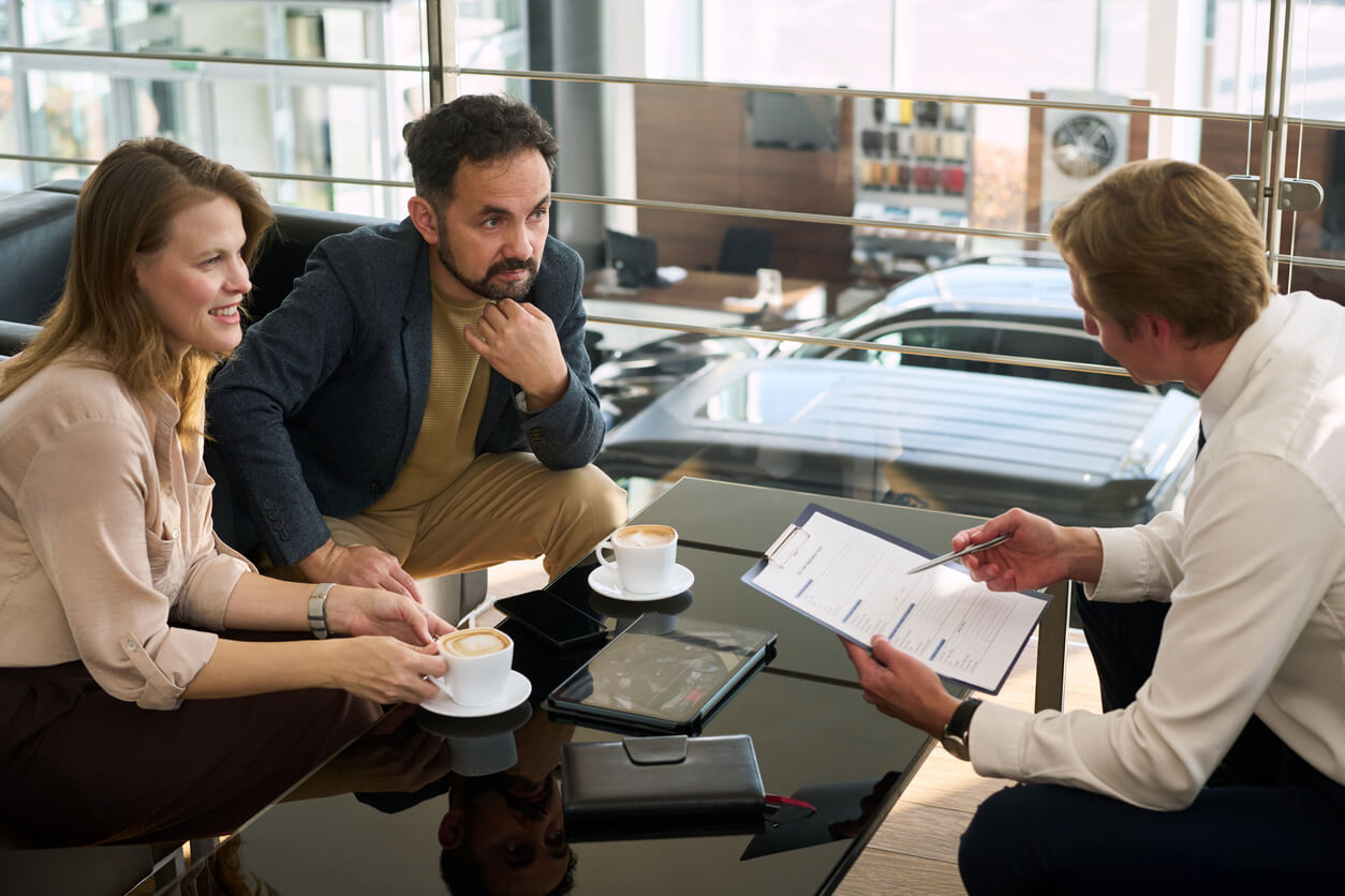 A couple reviewing a rent-to-own application form with a car dealer in a showroom