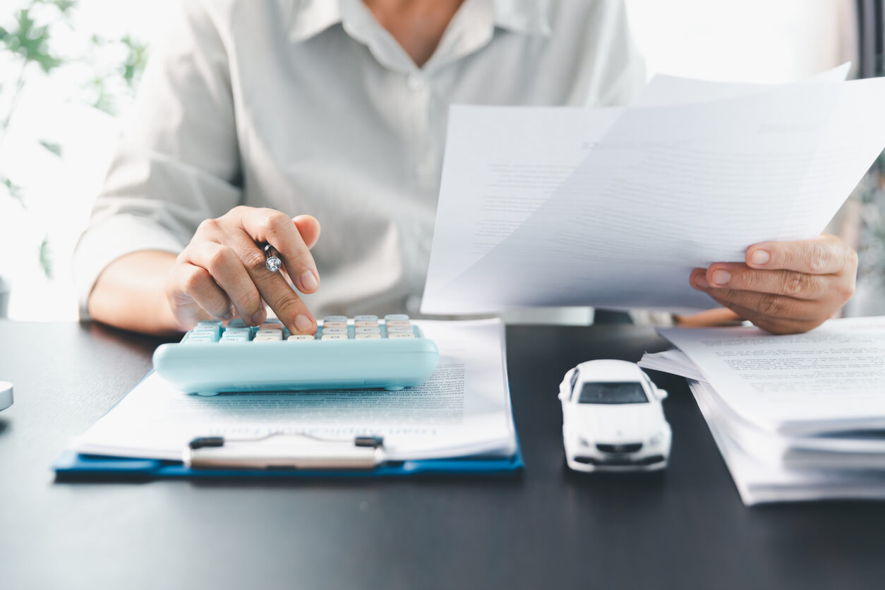 Person using a calculator to work out a weekly car budget, with a small model car on the desk