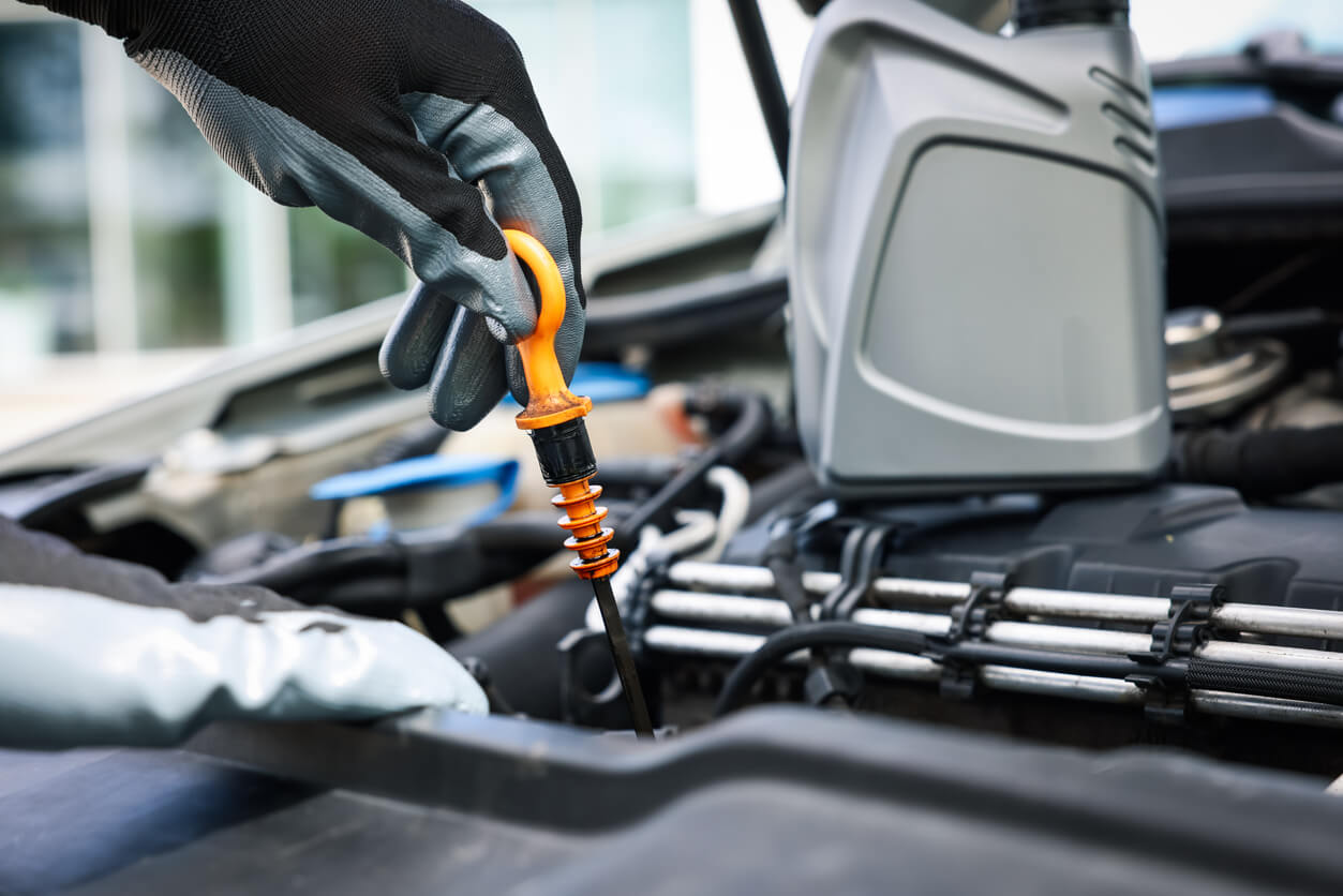 Gloved hand checking the engine oil level with a dipstick under a car bonnet