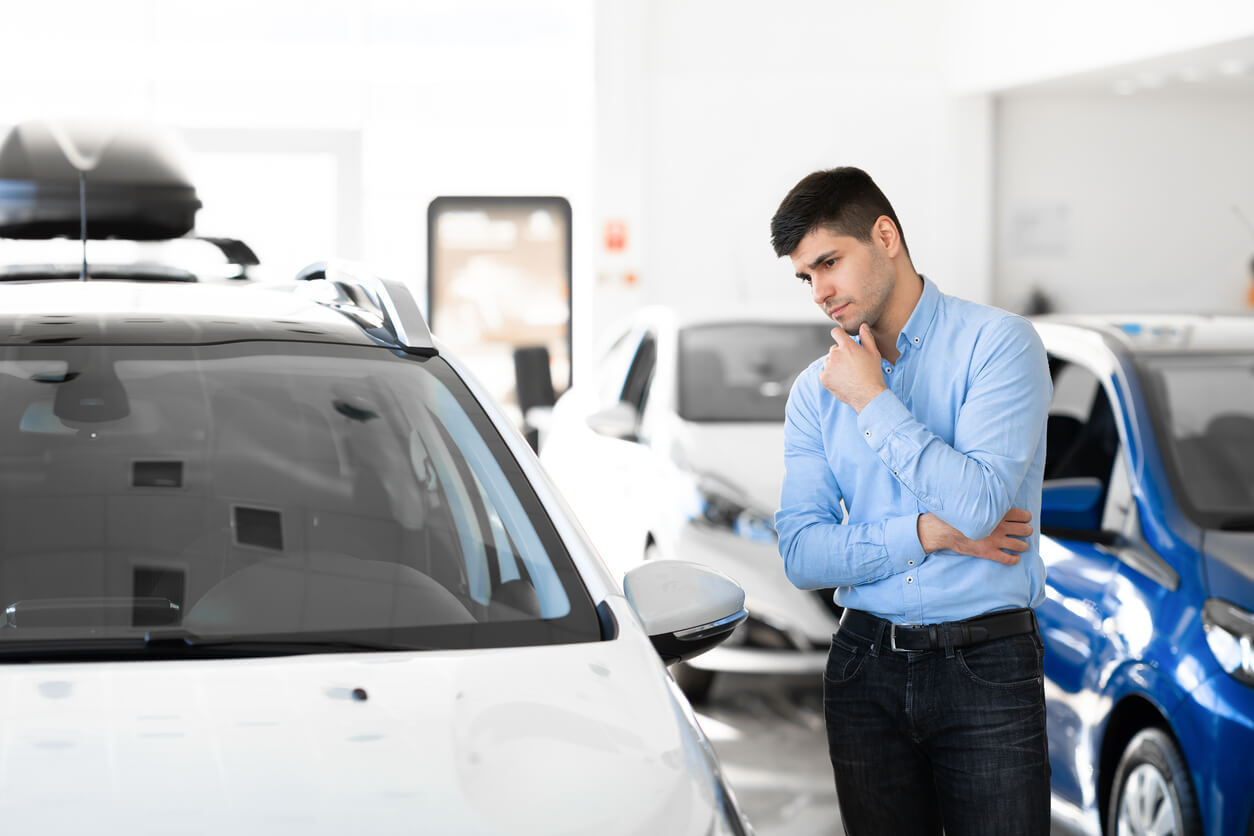 Man in a car showroom looking thoughtfully at a white car while weighing up his options